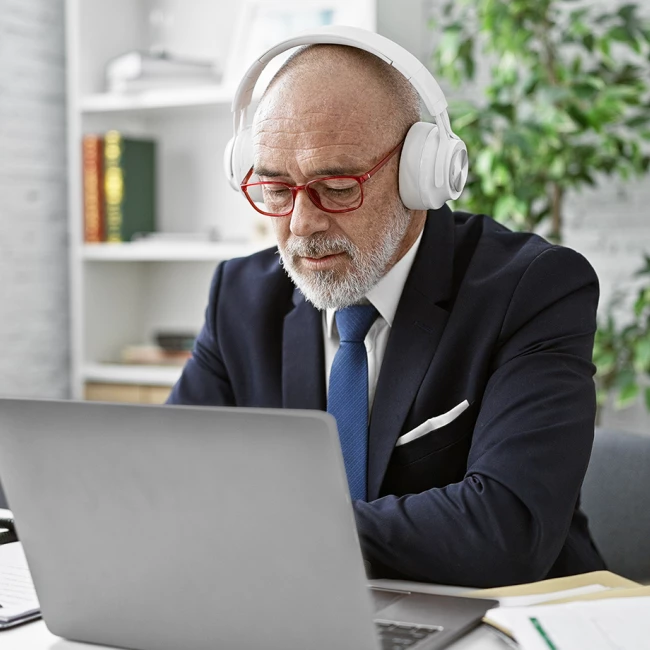 An older man in a suit wearing headphones, focused on working